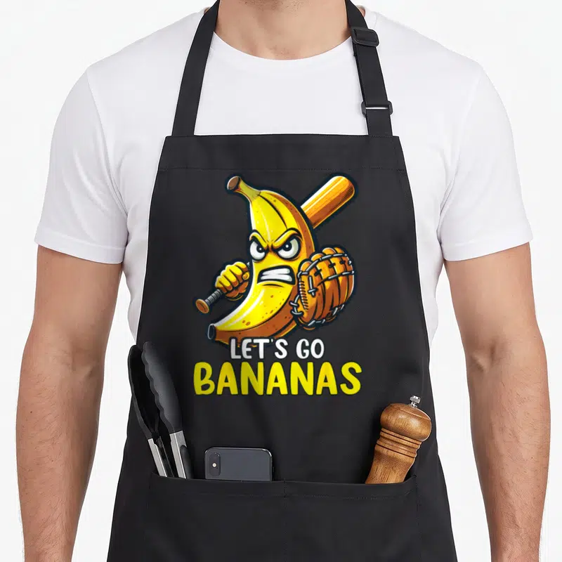 Baseball banana apron - Angry cartoon banana holding bat and glove below stacked LET'S GO BANANAS text in yellow — shown on a black cotton canvas apron against a white background