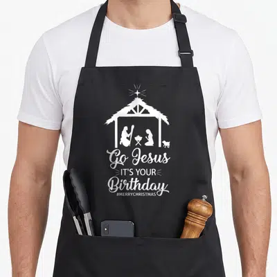 Birthday womens christmas apron - White nativity silhouette with Go Jesus IT'S YOUR Birthday text and star — shown on a black cotton canvas apron against a white background