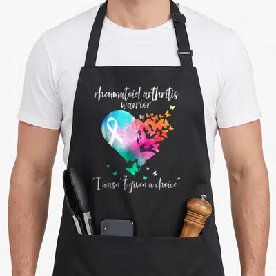 Arthritis warrior ribbon apron - Watercolor heart with white ribbon, heartbeat line, and butterflies in blue pink orange — shown on a black cotton canvas apron against a white background