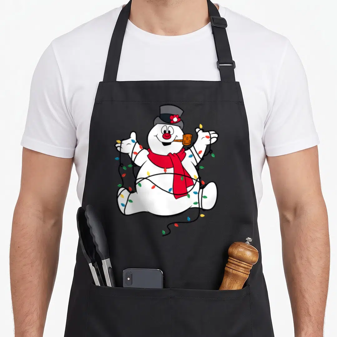 Portrait christmas snowman apron - Cartoon snowman sitting with red scarf, orange pipe, wrapped in multicolored — shown on a black cotton canvas apron against a white background