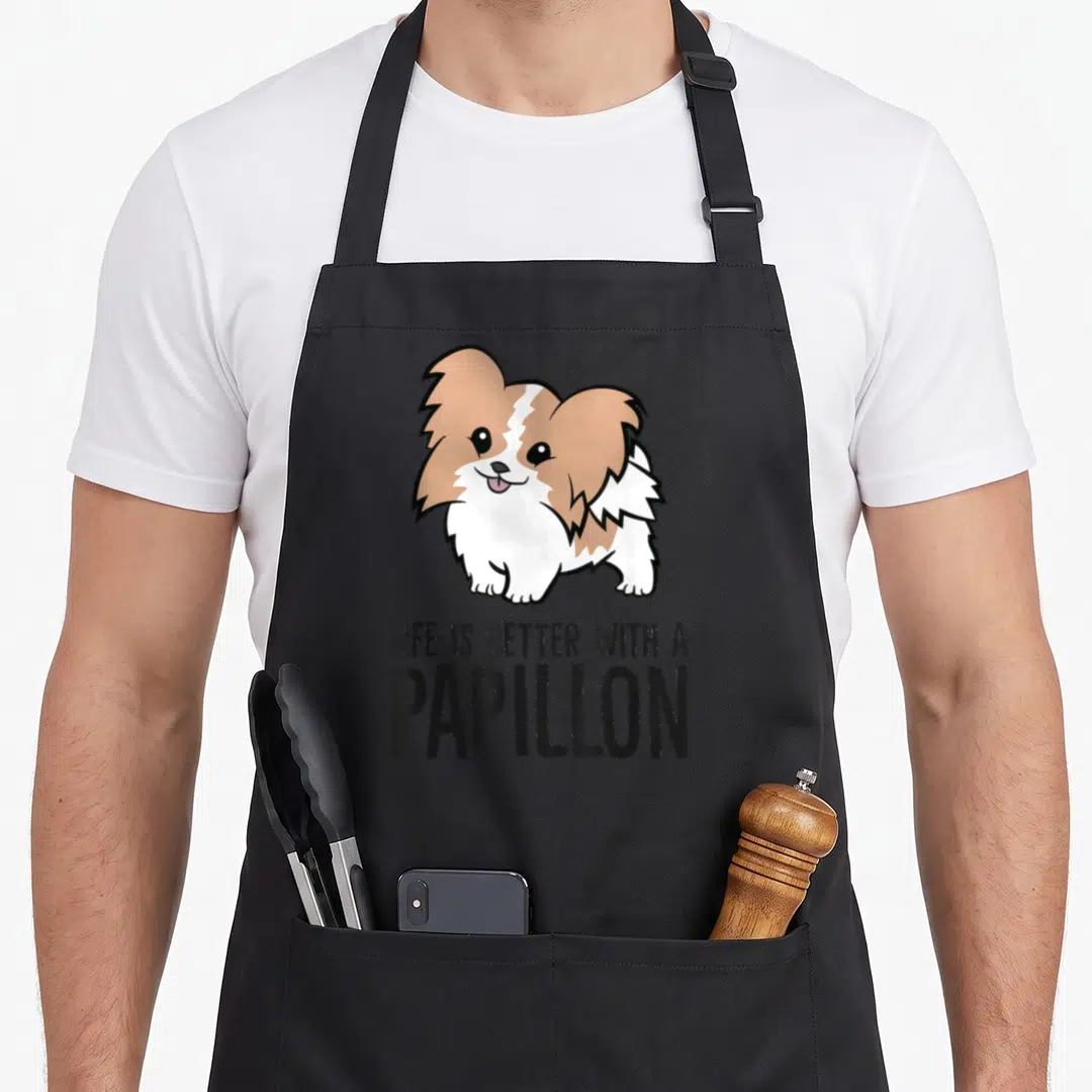 Better alma mater apron - Cartoon Papillon dog above LIFE IS BETTER WITH A PAPILLON text in brown white black — shown on a black cotton canvas apron against a white background