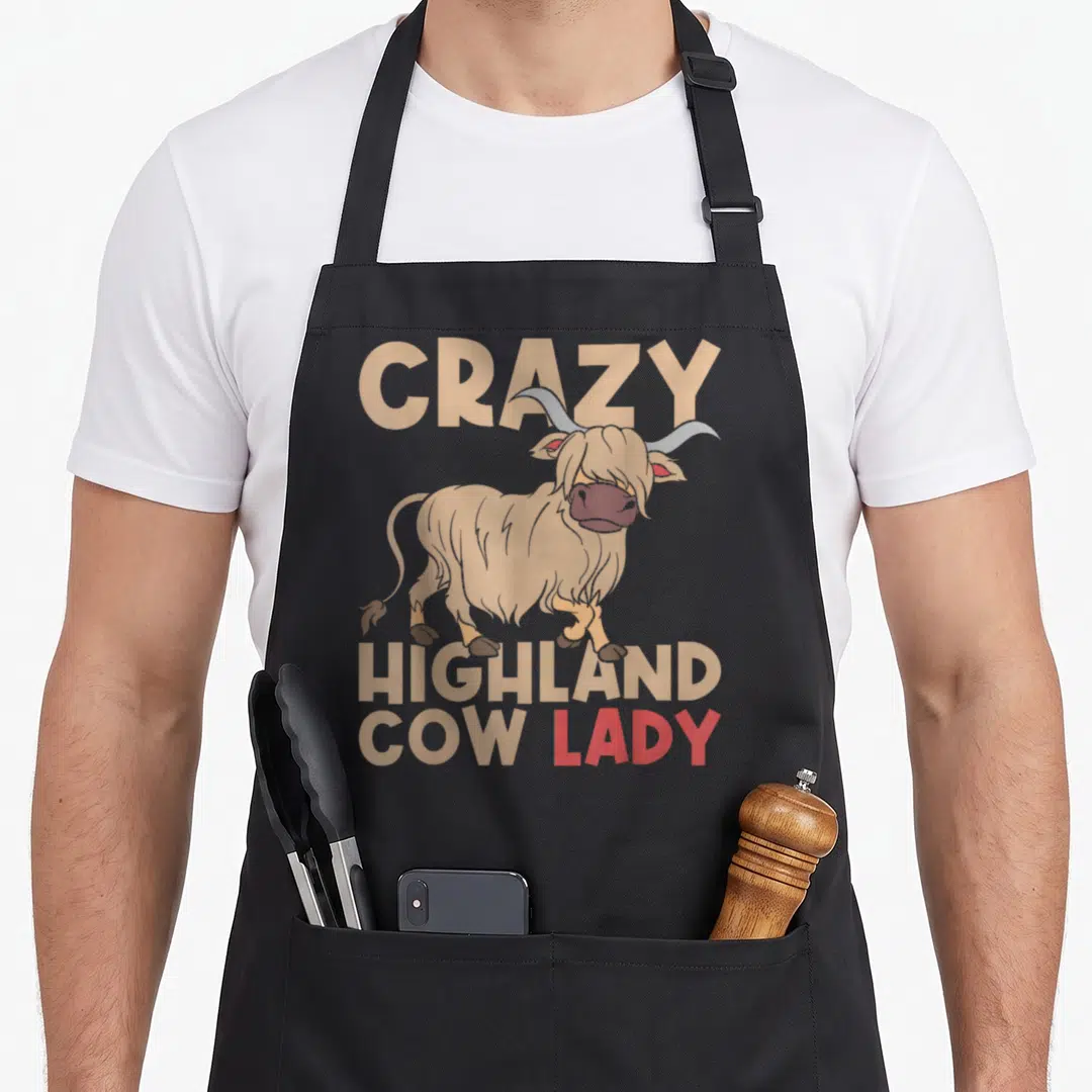 Farmer scottish cow print aprons - Cartoon highland cow illustration with beige and red text reading Crazy Highland Cow — shown on a black cotton canvas apron against a white background