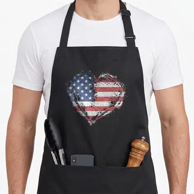 Shape american flag apron - Distressed heart shape filled with red white and blue flag pattern on stiff cotton canvas — shown on a black cotton canvas apron against a white background