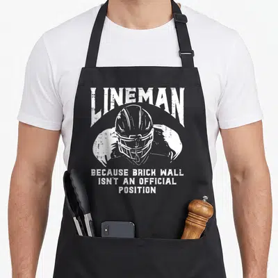 Brick football apron - White distressed lineman helmet graphic with sarcastic quote text — shown on a black cotton canvas apron against a white background