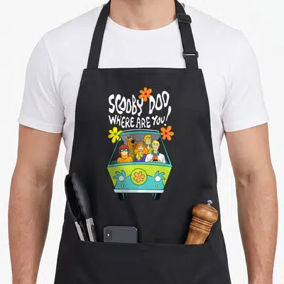 Floral machine apron - Cartoon van with five characters and flowers under white text SCOOBY DOO WHERE ARE YOU — shown on a black cotton canvas apron against a white background