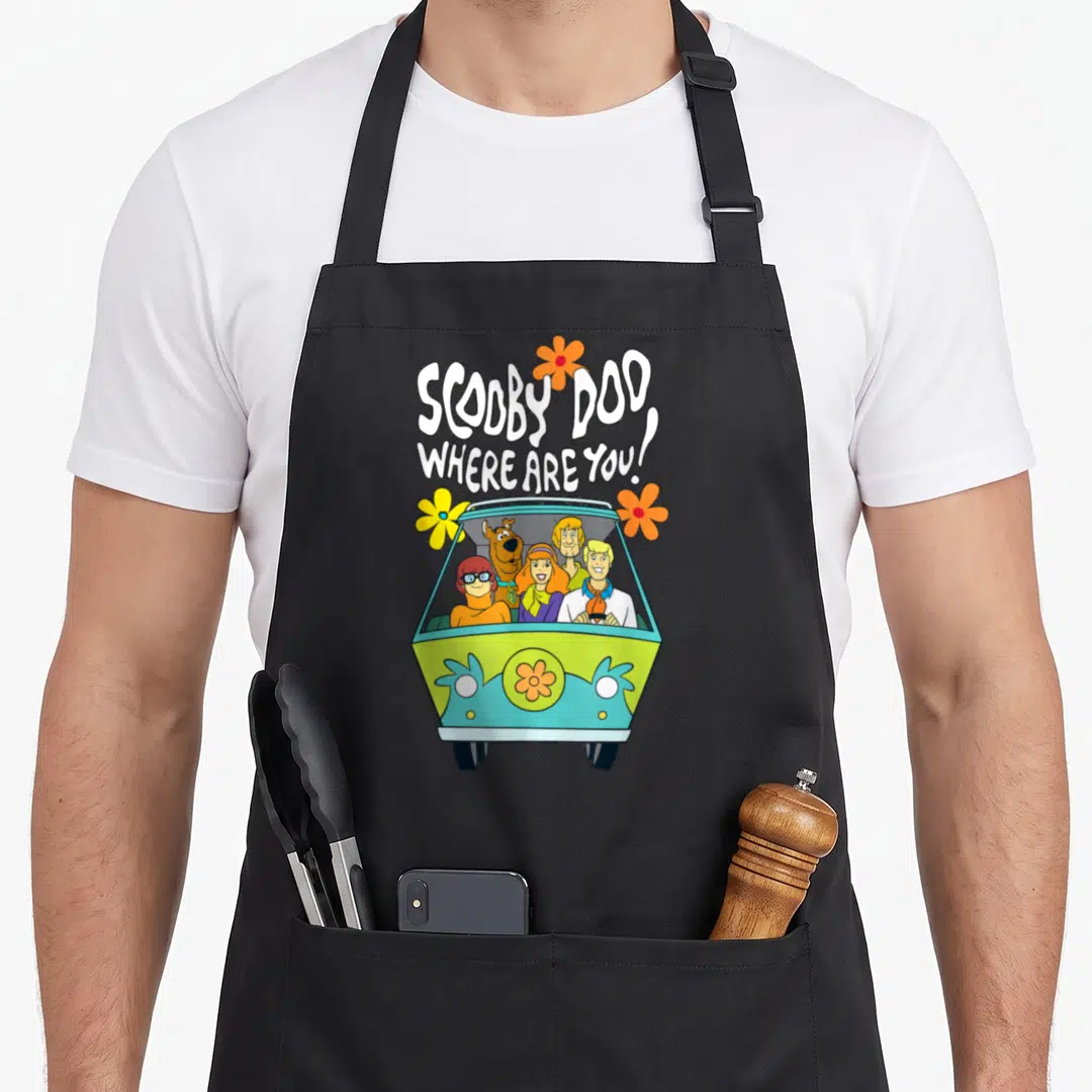 Floral machine apron - Cartoon van with five characters and flowers under white text SCOOBY DOO WHERE ARE YOU — shown on a black cotton canvas apron against a white background