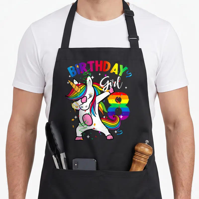 8th dabbing birthday apron - Cartoon white unicorn dabbing next to rainbow number 8 and BIRTHDAY Girl text — shown on a black cotton canvas apron against a white background