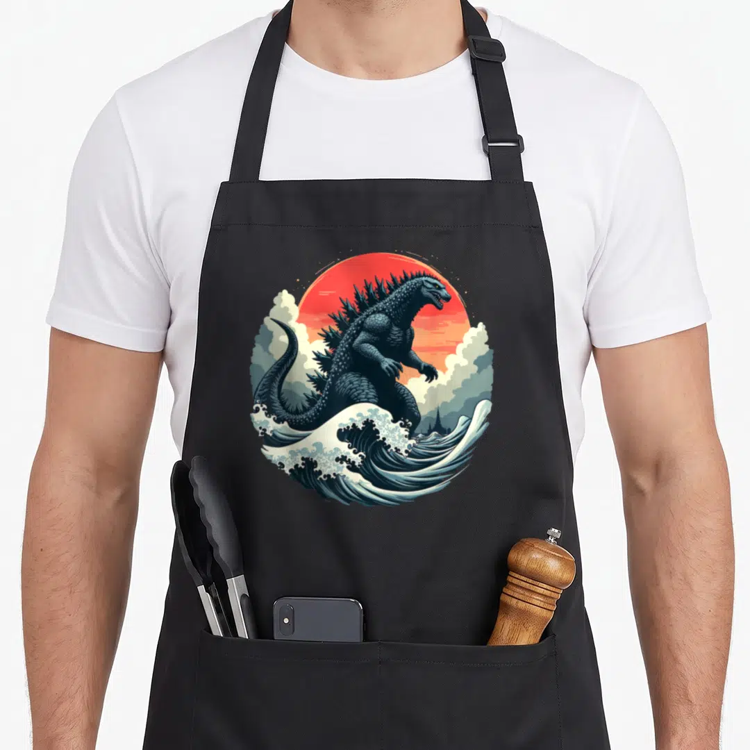 Japanese wave apron - Retro kaiju monster rising from blue waves against a red sun with grey clouds — shown on a black cotton canvas apron against a white background