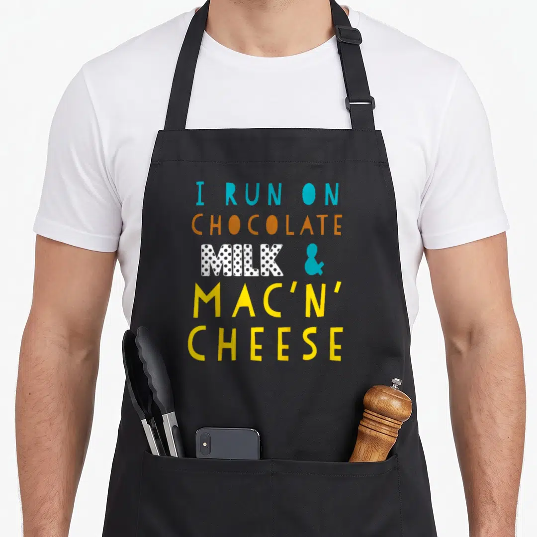 Run mac apron - Stacked text I RUN ON CHOCOLATE MILK & MAC'N' CHEESE in blue brown white and yellow — shown on a black cotton canvas apron against a white background