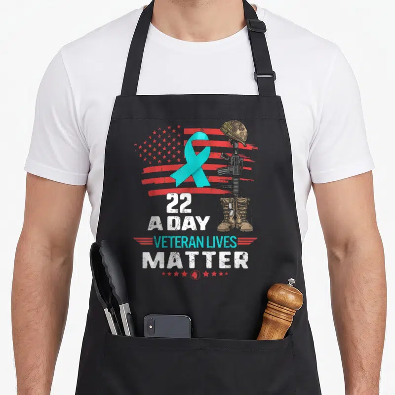 Matter american flag apron - Cyan ribbon and soldier cross over distressed flag with 22 A Day text — shown on a black cotton canvas apron against a white background