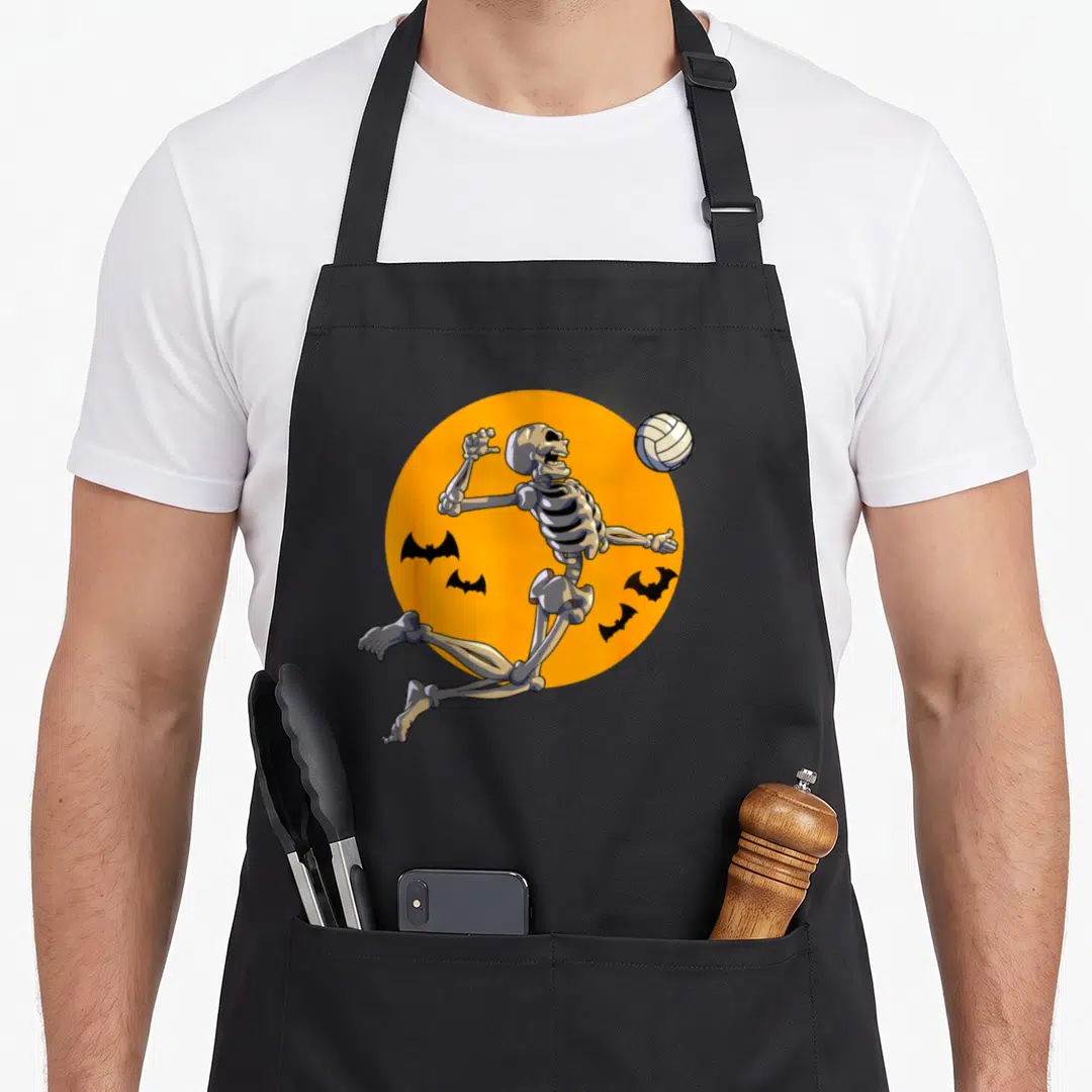 Volleyball halloween apron - Cartoon skeleton jumping for a volleyball inside an orange circle with four black bats — shown on a black cotton canvas apron against a white background