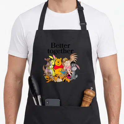 Better friends cooking apron - Winnie the Pooh and friends standing together under Better Together text — shown on a black cotton canvas apron against a white background