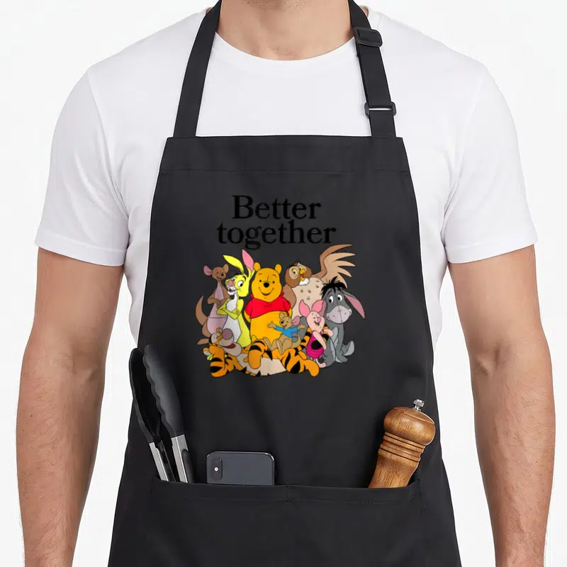 Better friends cooking apron - Winnie the Pooh and friends standing together under Better Together text — shown on a black cotton canvas apron against a white background