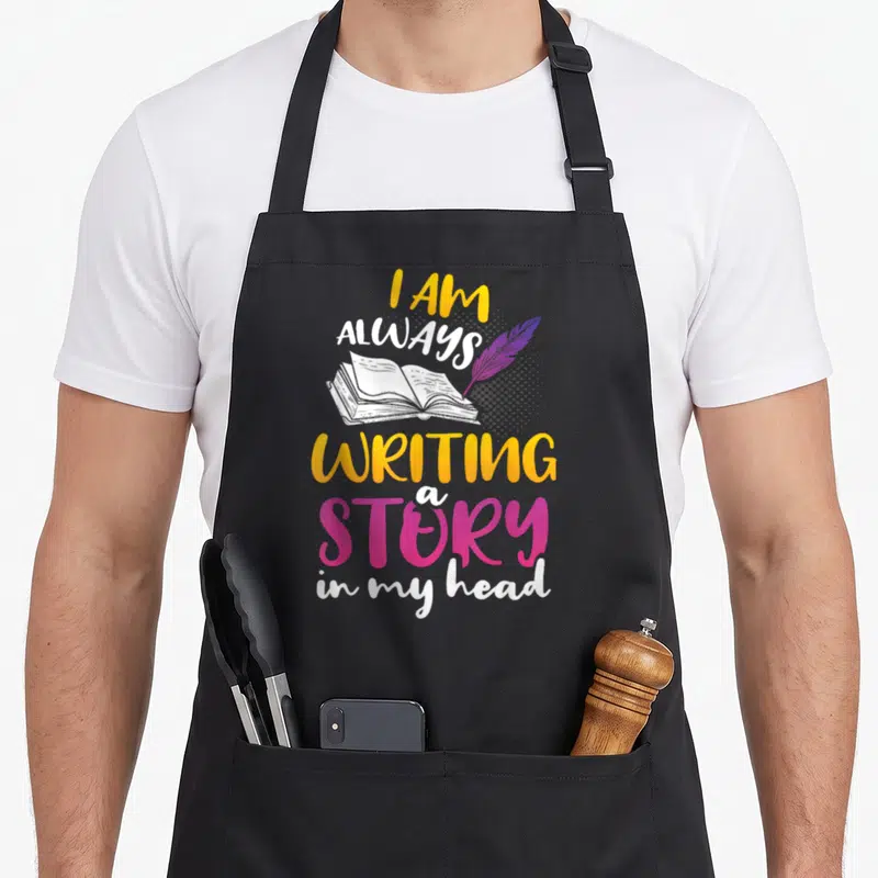 Book publisher apron - I AM ALWAYS WRITING a STORY in my head text with open book and purple feather — shown on a black cotton canvas apron against a white background