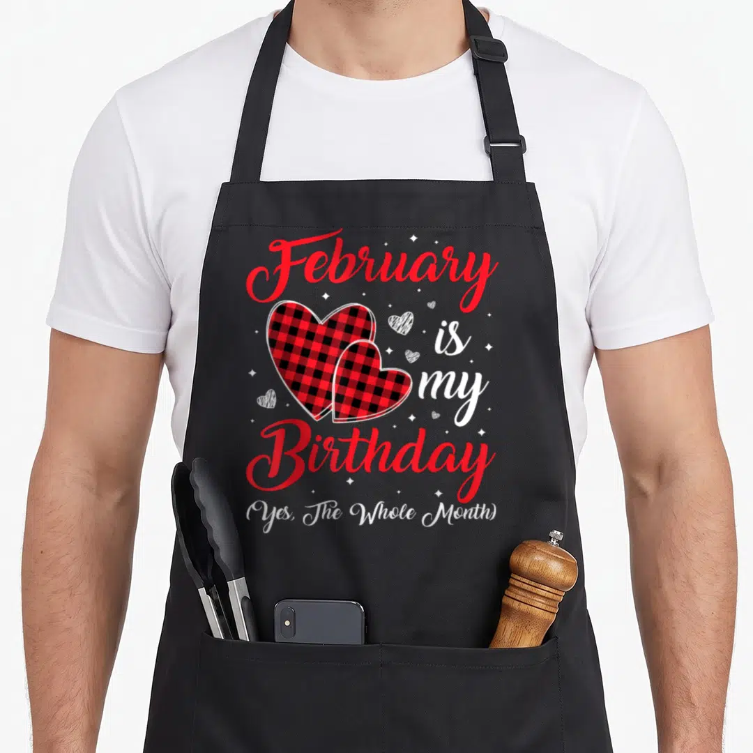 February whole birthday apron - Red plaid hearts and text February is my Birthday Yes The Whole Month — shown on a black cotton canvas apron against a white background