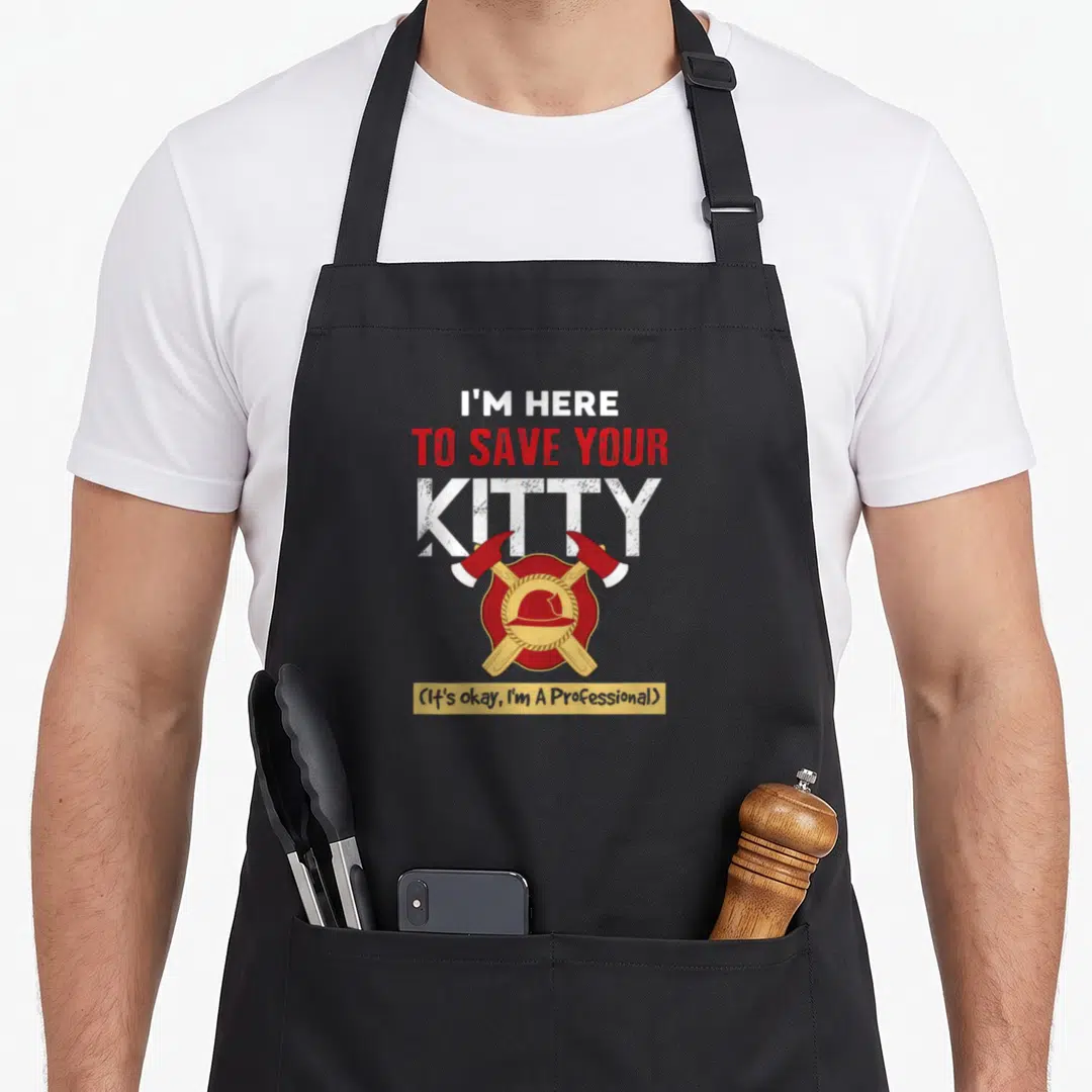 Save firefighter apron - I'M HERE TO SAVE YOUR KITTY text above red shield with helmet and crossed axes — shown on a black cotton canvas apron against a white background