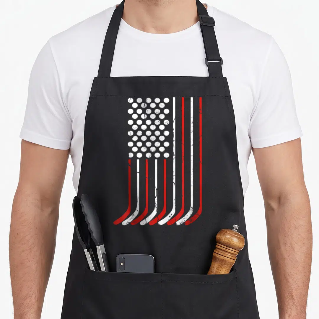 Hockey 4th of july apron - Red and white stylized flag formed by seven vertical hockey sticks and a grid of white — shown on a black cotton canvas apron against a white background