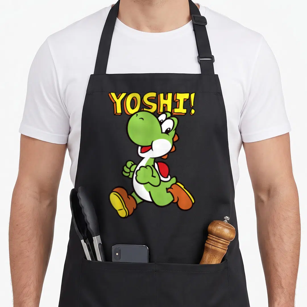 Intro jump apron - Arched YOSHI! text above a walking green cartoon dinosaur with white belly — shown on a black cotton canvas apron against a white background