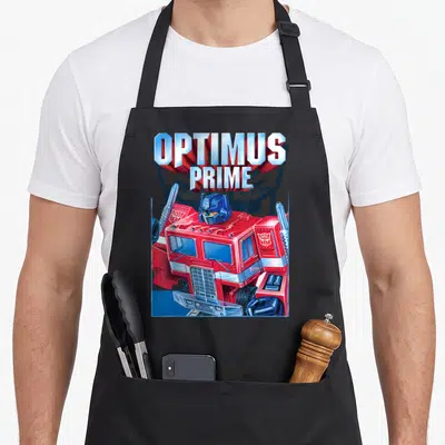 Funny portrait transformer apron - OPTIMUS PRIME 3D text above red blue silver cartoon truck cab facing forward — shown on a black cotton canvas apron against a white background