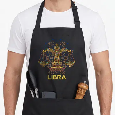 Vintage libra zodiac aprons - Ornate Libra scales in yellow and red before a blue zodiac wheel with LIBRA text below — shown on a black cotton canvas apron against a white background