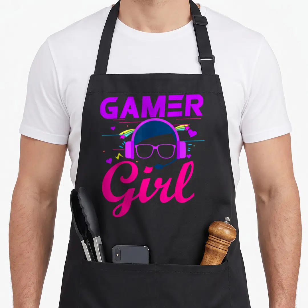 Family video game apron - Gamer Girl text with cartoon avatar wearing headset glasses surrounded by rainbow stars — shown on a black cotton canvas apron against a white background