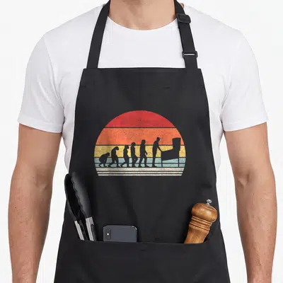 Pinball catch some rays apron - Six grey hominid silhouettes evolving into arcade player inside red orange yellow — shown on a black cotton canvas apron against a white background