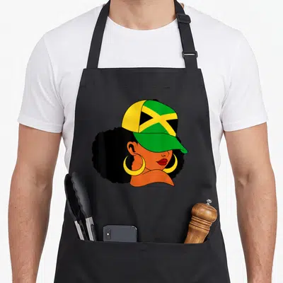 Afro patriotic aprons - Cartoon woman with afro hair wearing a green yellow and black flag cap and gold hoop earrings — shown on a black cotton canvas apron against a white background