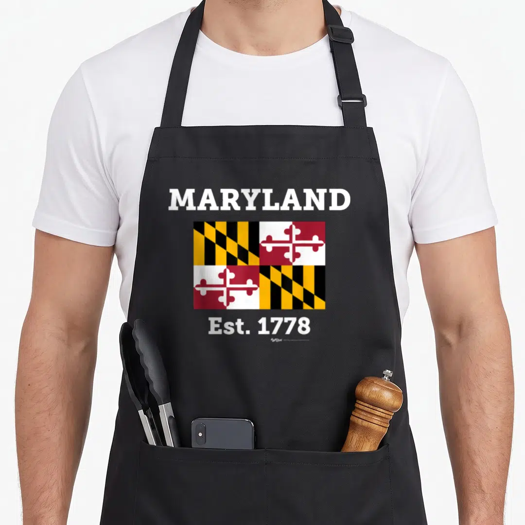 Est maryland eastern apron - MARYLAND Est. 1778 text above and below Maryland state flag in red, white, black — shown on a black cotton canvas apron against a white background