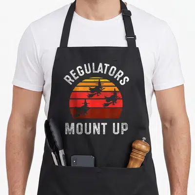 Regulator halloween witch apron - Retro striped sun with four grey witch silhouettes and REGULATORS MOUNT UP text — shown on a black cotton canvas apron against a white background