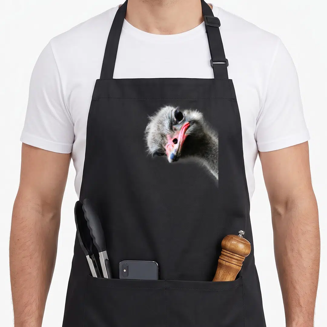 Dibble ostrich lover apron - Realistic photo of an ostrich head with a pink beak on a grey background — shown on a black cotton canvas apron against a white background