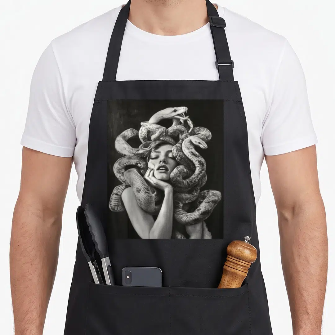 Snake gothic apron - Black and white photo of a woman with coiled snakes forming her hair around her face — shown on a black cotton canvas apron against a white background
