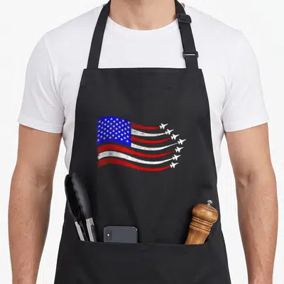Waving 4th of july apron - Distressed USA flag with six white planes leaving red and white smoke trails — shown on a black cotton canvas apron against a white background