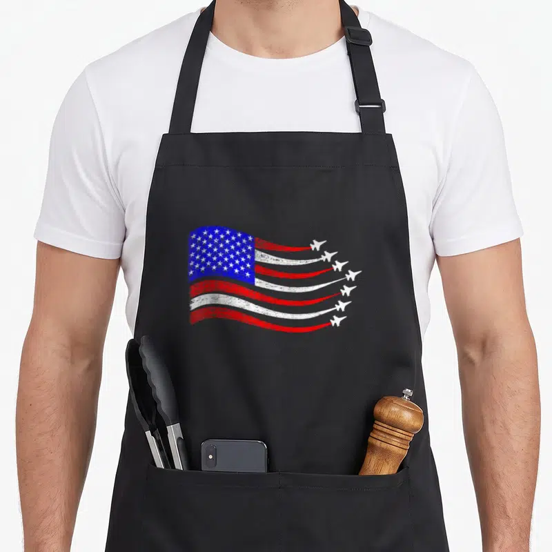 Waving 4th of july apron - Distressed USA flag with six white planes leaving red and white smoke trails — shown on a black cotton canvas apron against a white background