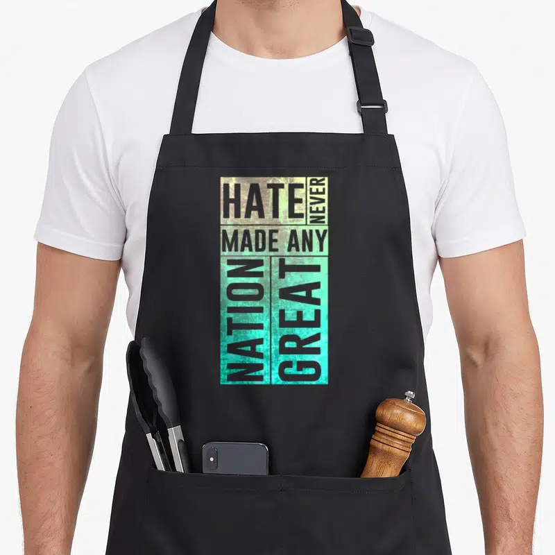 Immigrant pro apron - Stacked grey text reading Hate Never Made Any Nation Great on teal and yellow background — shown on a black cotton canvas apron against a white background