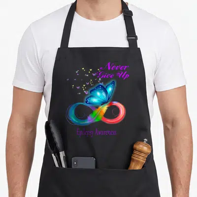 Epilepsy awareness butterfly apron - Blue butterfly on rainbow infinity symbol with purple Never Give Up text — shown on a black cotton canvas apron against a white background