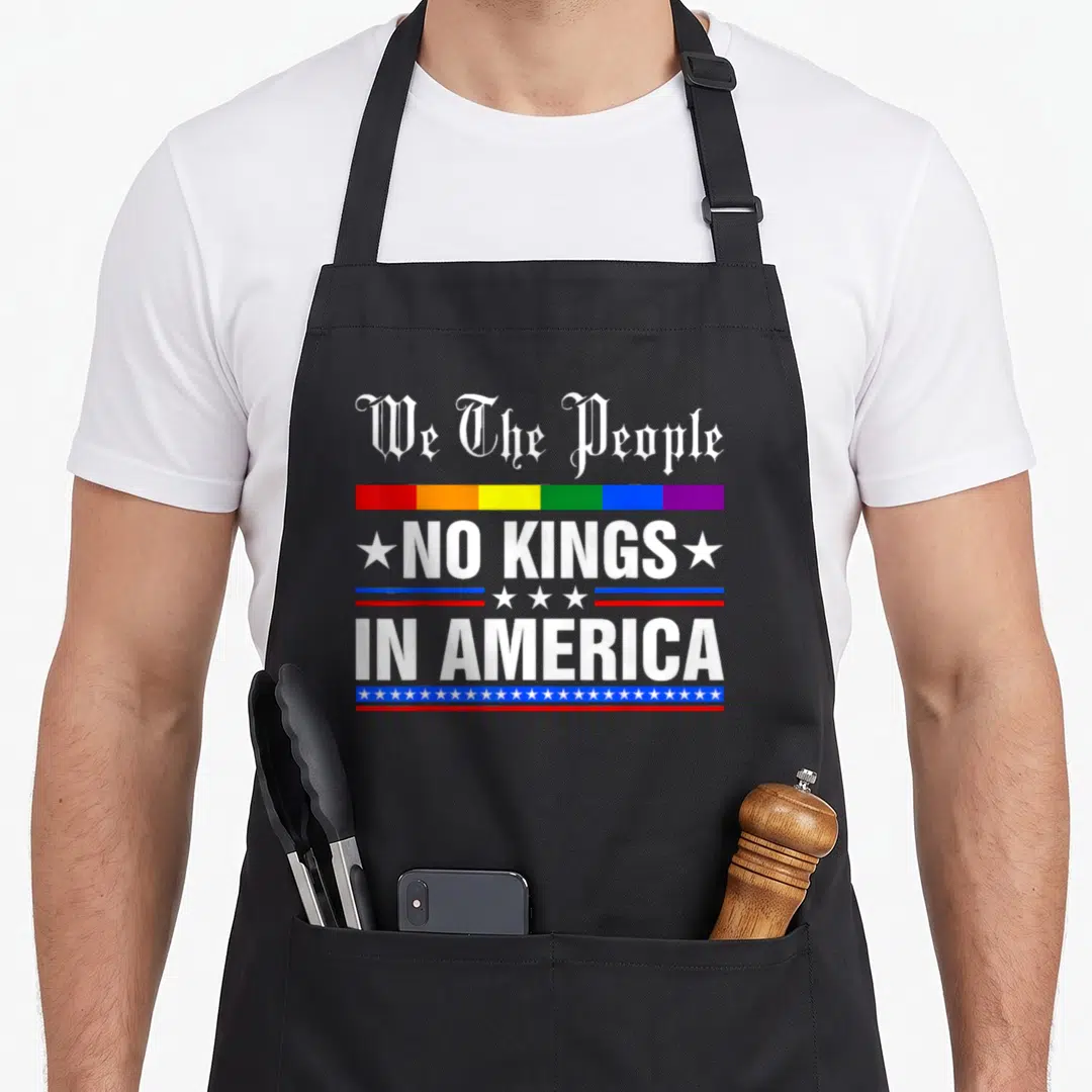 Political king apron - Stacked We The People NO KINGS IN AMERICA text with rainbow bar and star dividers in red blue — shown on a black cotton canvas apron against a white background
