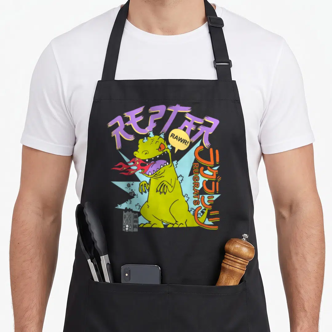 Breathing fire apron - Lime green dinosaur breathing fire with purple REPTAR text and Japanese katakana characters — shown on a black cotton canvas apron against a white background