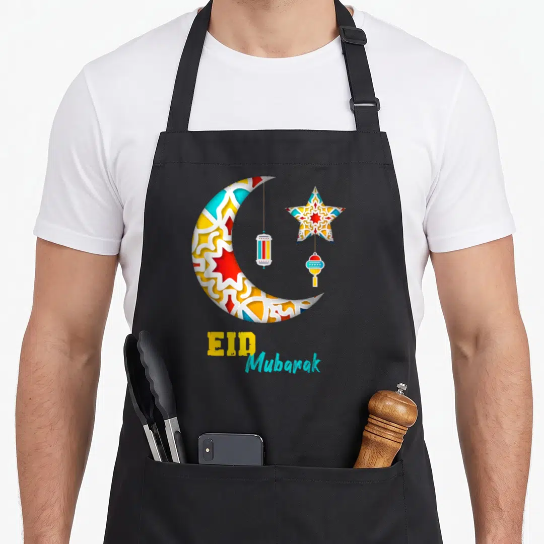 Alfitr eid apron - Patterned crescent moon star and two lanterns with EID Mubarak text — shown on a black cotton canvas apron against a white background