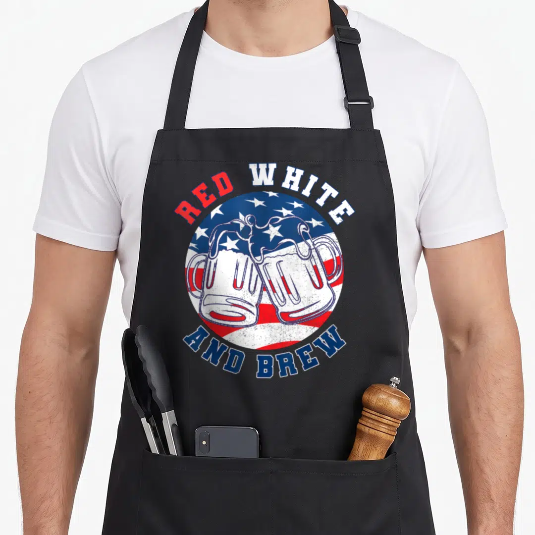 Beer merica 4th of july apron - Two beer mugs clinking in front of circular USA flag with red white and blue text — shown on a black cotton canvas apron against a white background