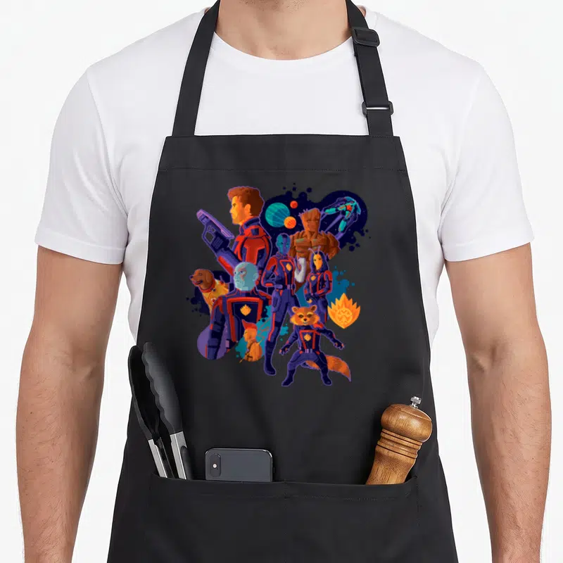 Cosmic galaxies apron - Guardians of the Galaxy team in blue, red, purple, and orange cartoon style with planets — shown on a black cotton canvas apron against a white background