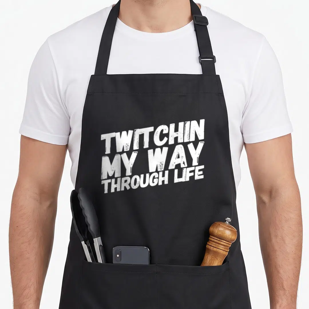 Twitchin tourette awareness apron - White distressed text reading TWITCHIN MY WAY THROUGH LIFE stacked in three tilted — shown on a black cotton canvas apron against a white background