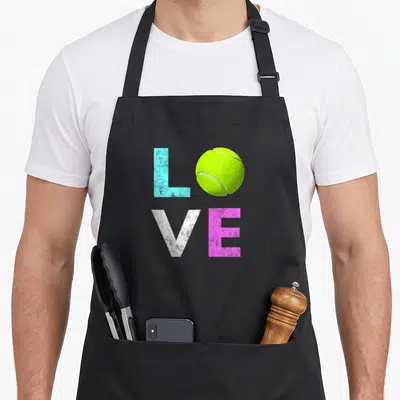 Tennis birthday apron - Colorful LOVE text with tennis ball replacing O in grid layout — shown on a black cotton canvas apron against a white background