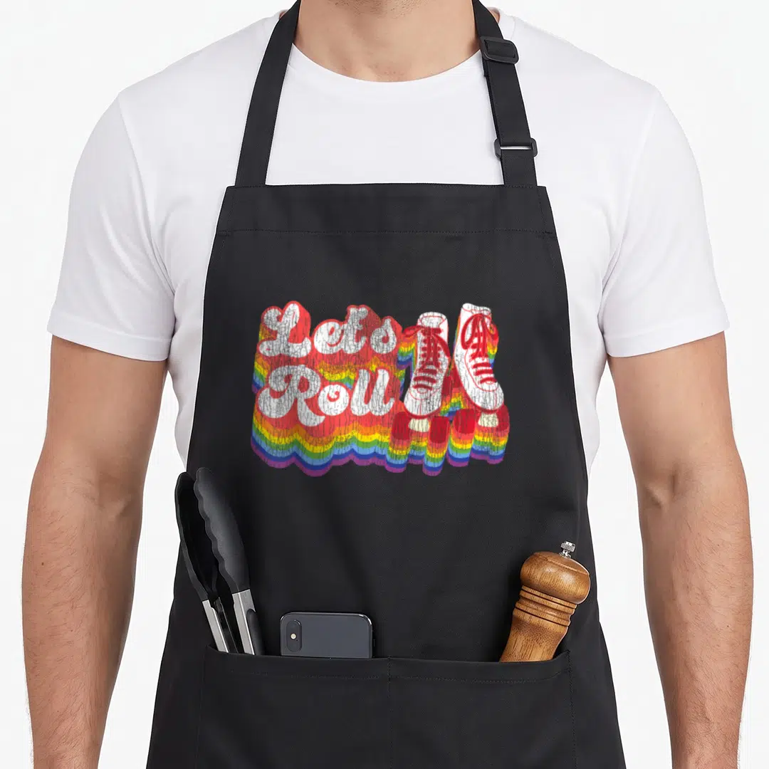 Roller 1970s apron - Let's Roll text and two white sneakers over rainbow waves — shown on a black cotton canvas apron against a white background