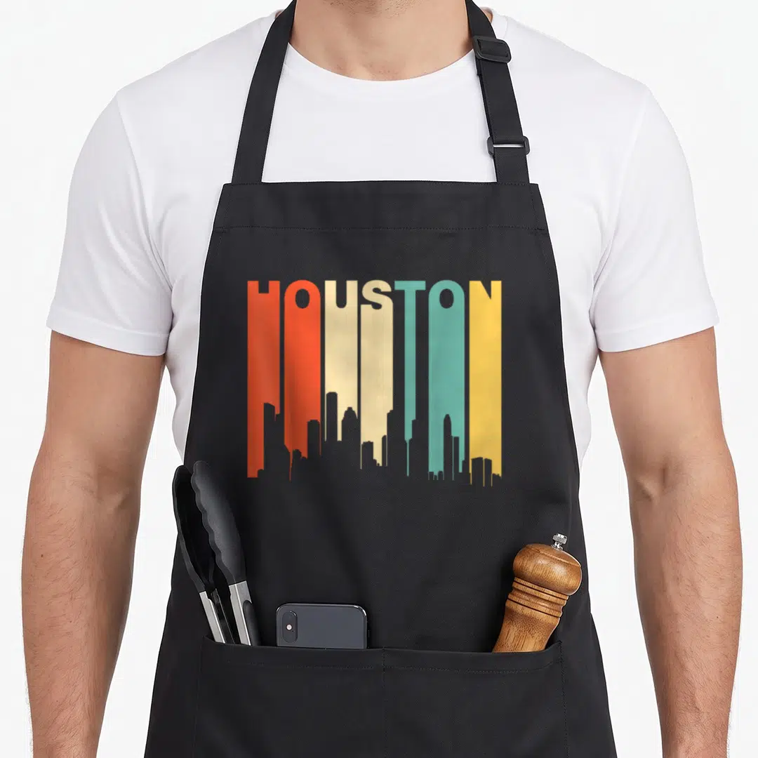 Houston texas apron - HOUSTON text forming colorful city skyline silhouette in retro red orange cream teal and yellow — shown on a black cotton canvas apron against a white background