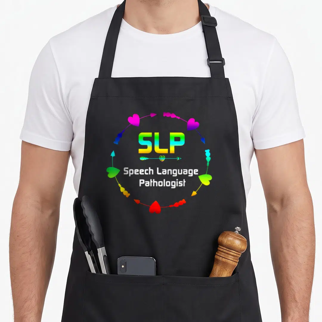 Slp speech my therapy apron - SLP text surrounded by rainbow heart arrows and Speech Language Pathologist words — shown on a black cotton canvas apron against a white background