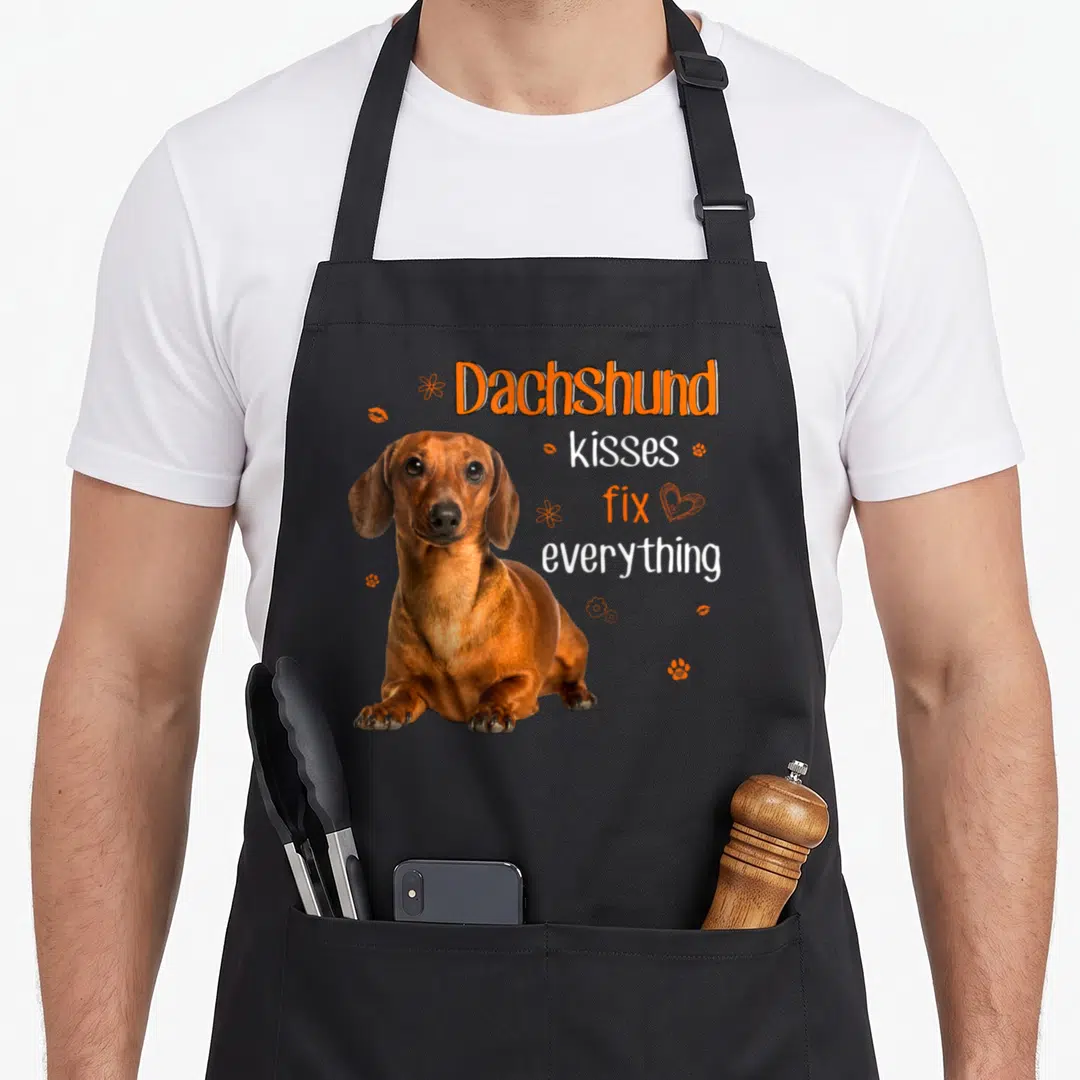 Kiss dachshund apron - Brown dachshund photo with orange flowers lips and text Dachshund kisses fix everything — shown on a black cotton canvas apron against a white background