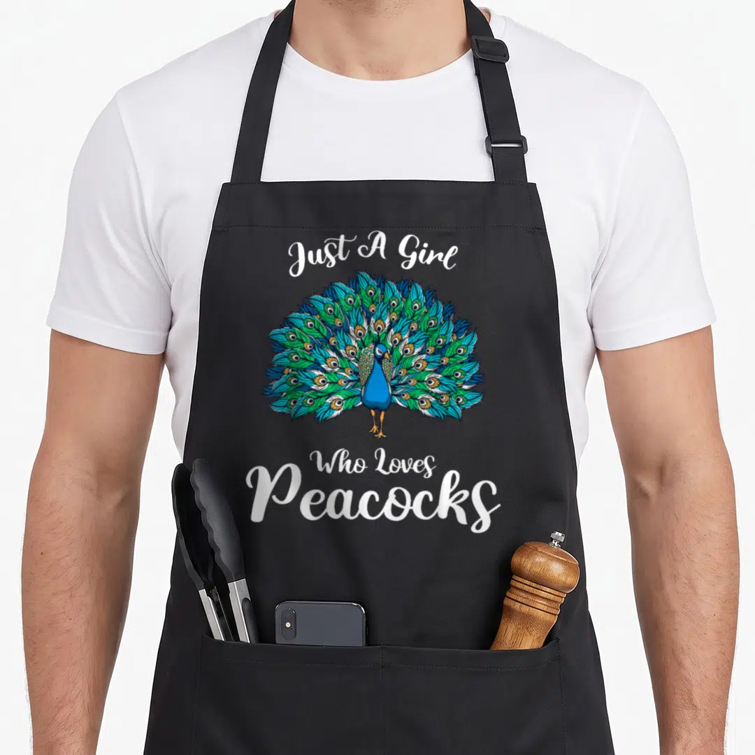 Animal apron with pockets for women - Cartoon peacock with blue and green tail feathers and white script text — shown on a black cotton canvas apron against a white background