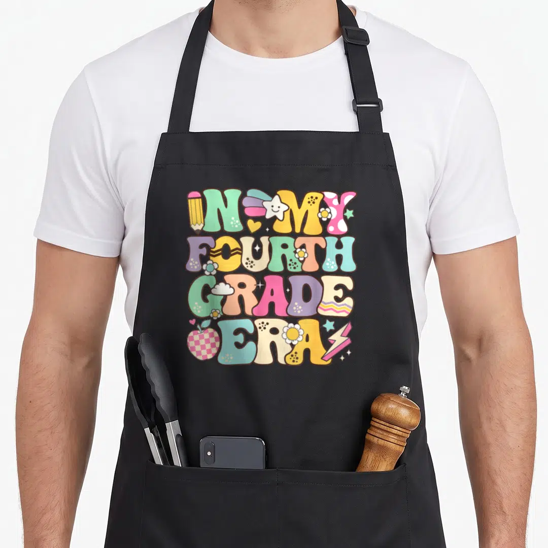 Era groovy grade apron - Stacked retro text IN MY FOURTH GRADE ERA with colorful pencil, apple, stars and flowers — shown on a black cotton canvas apron against a white background
