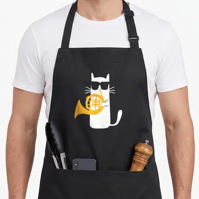 French cat apron - White cat with black sunglasses holding an orange french horn on a black bib — shown on a black cotton canvas apron against a white background