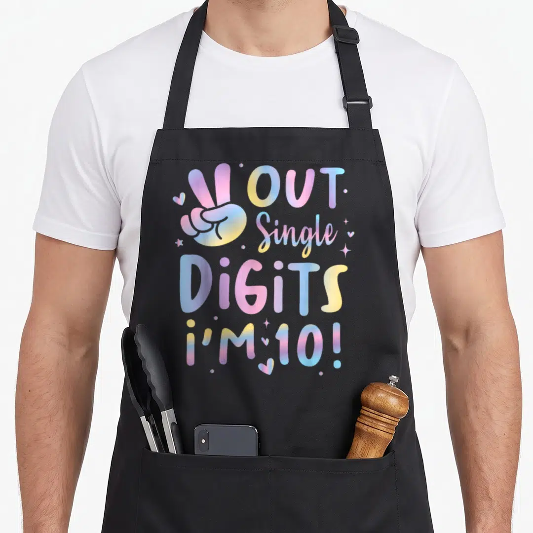 Peace birthday apron - Hand peace sign with OUT Single DiGiTS i'M 10! text in pastel gradient colors — shown on a black cotton canvas apron against a white background